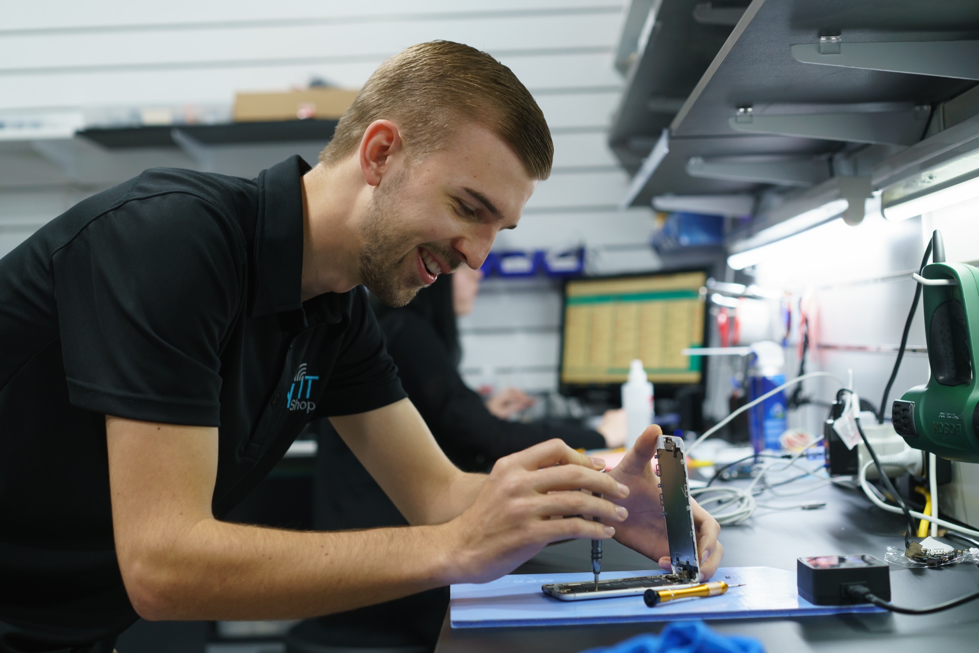 My IT Shop technician smiling while repairing a phone at the workbench