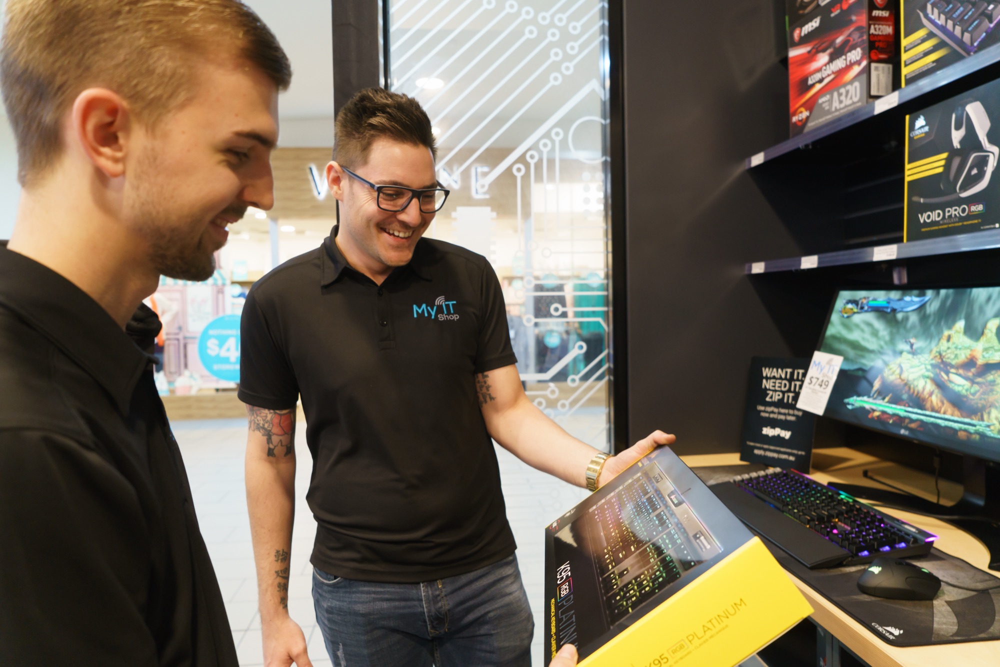 Two My IT Shop team members smiling while looking at a keyboard in store